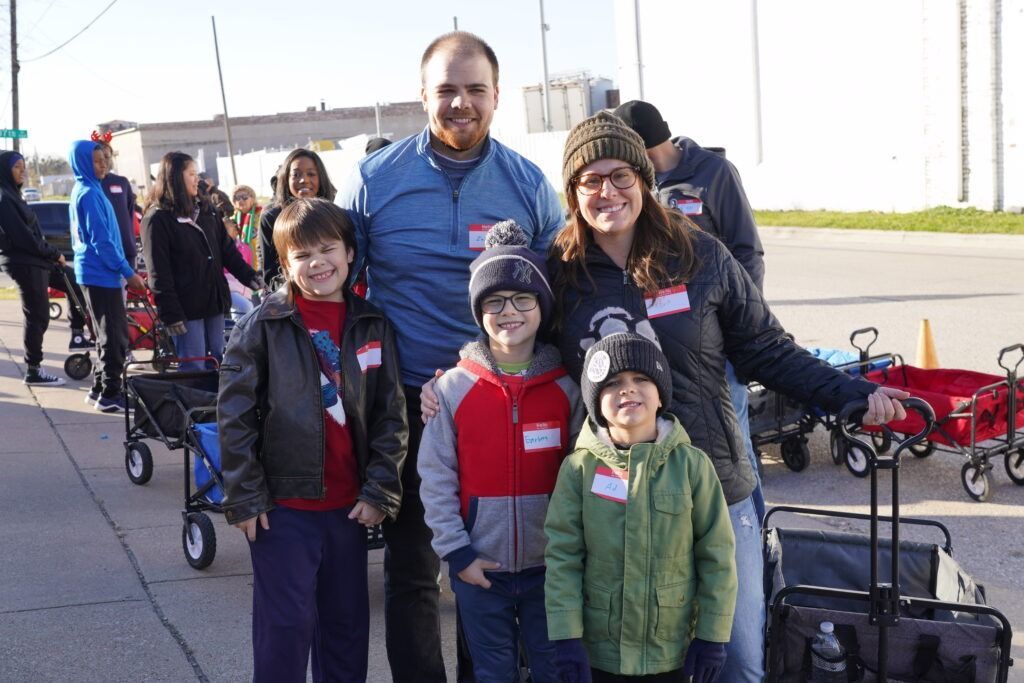 Family standing outdoors with strollers and carts near a waterfront, smiling at the camera