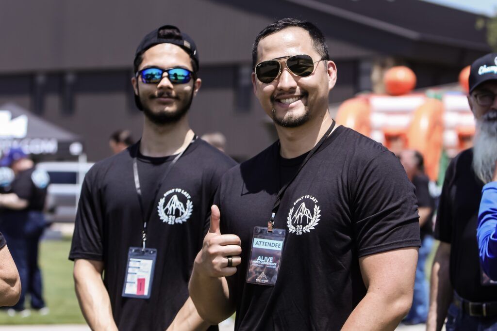 Two men in black shirts and sunglasses smiling and posing outdoors at an event