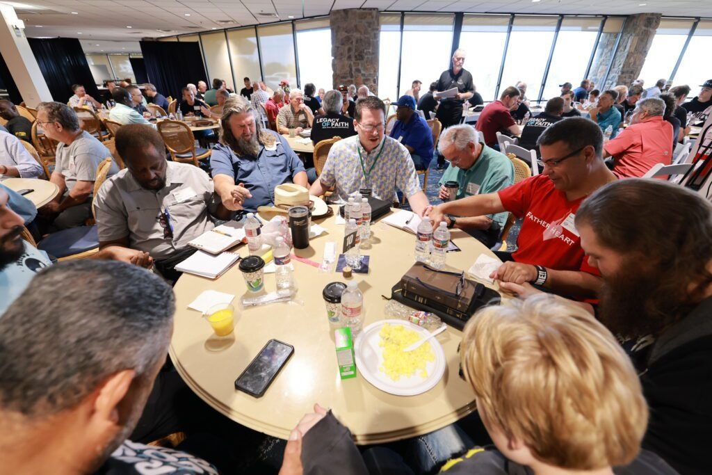 People gathered around a round table, eating and talking in a bright cafeteria.