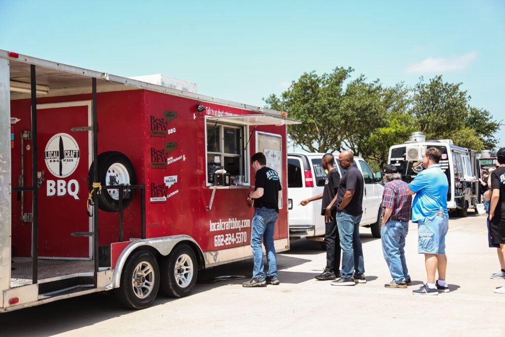 Red BBQ food truck serving people in a sunny parking lot