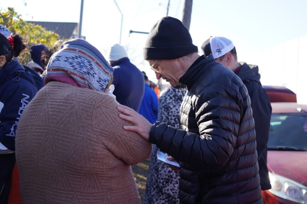 Two people in winter hats and jackets talking outdoors near parked cars