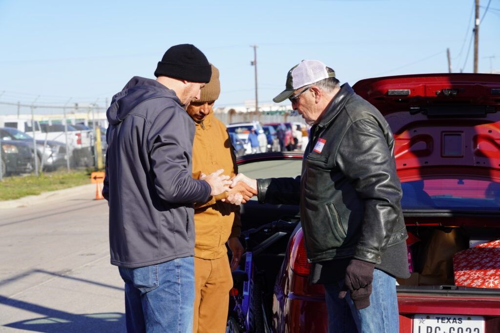 Three people stand by a red truck, looking at papers in a parking lot.