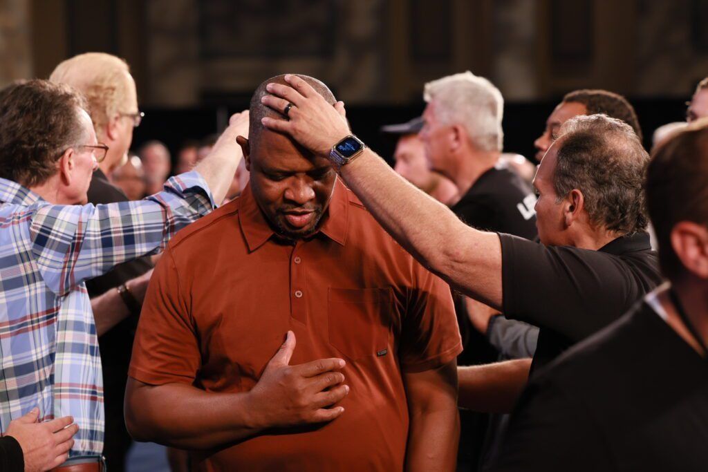 People praying together, with hands on a man’s head in a church setting.