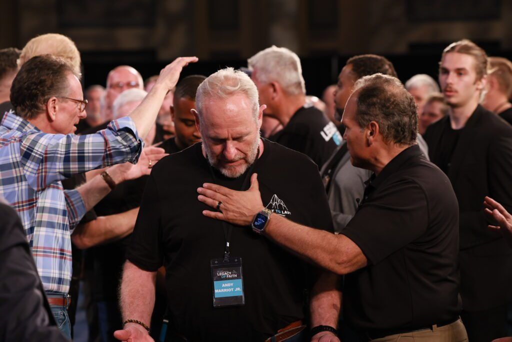 Several people gathered closely, comforting a man in a black shirt at an indoor event.