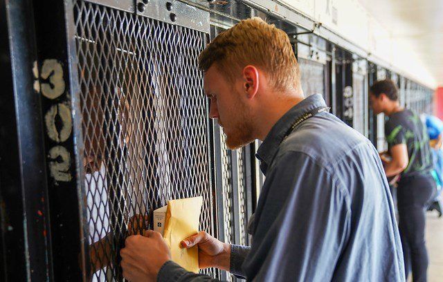 Man writing on a yellow form at a jail cell window behind a metal mesh door