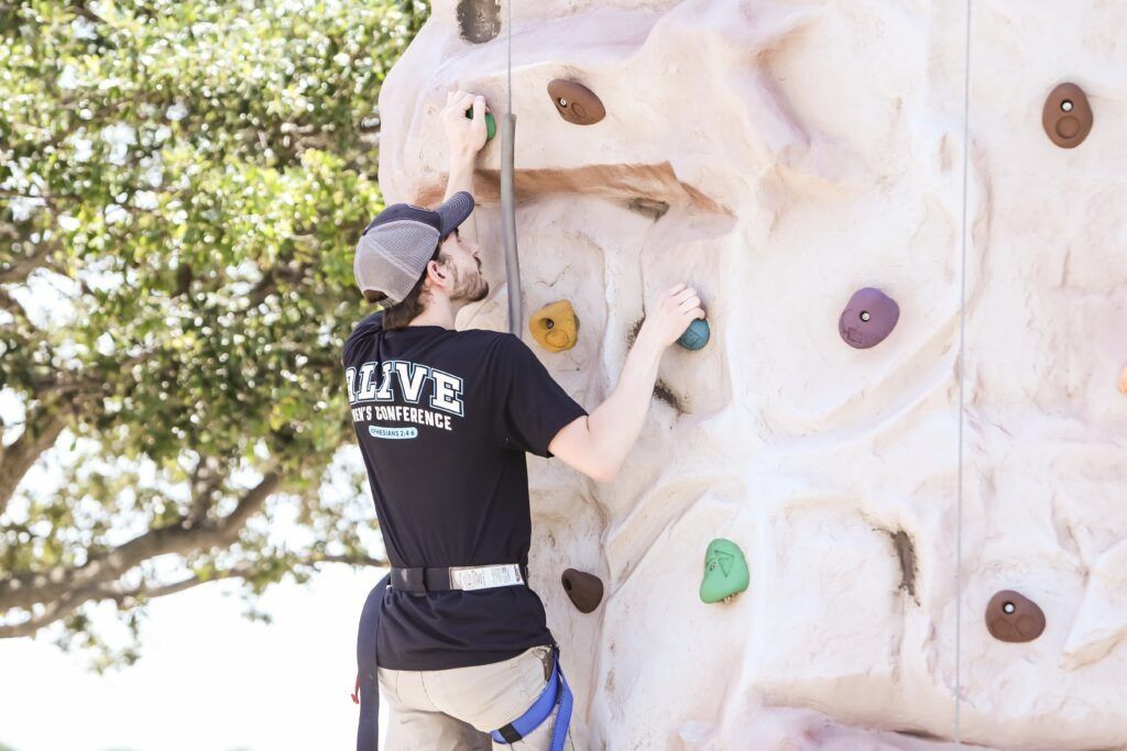 Person rock climbing on an outdoor wall with colorful holds.