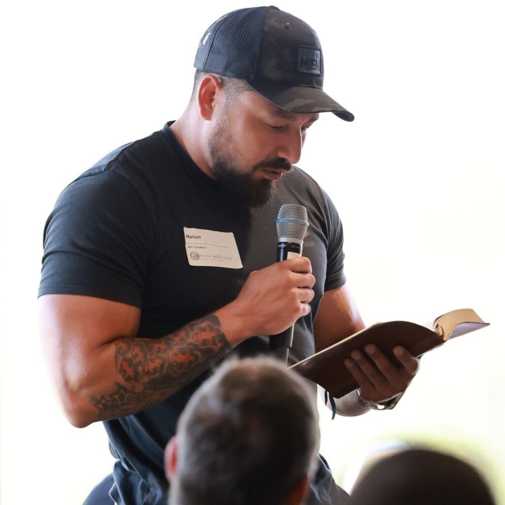 Man in black shirt reading from a book while holding a microphone at an event
