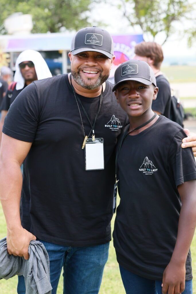 Two smiling men in black shirts and caps standing together outdoors at an event