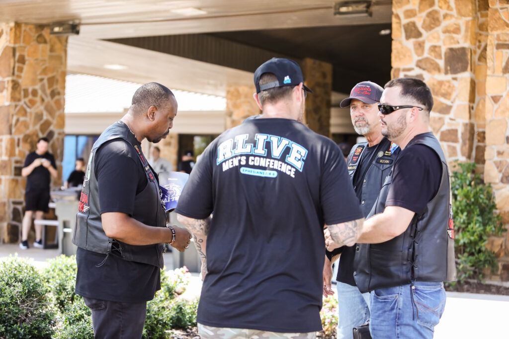 Four people in dark shirts talk outside a stone building entrance.