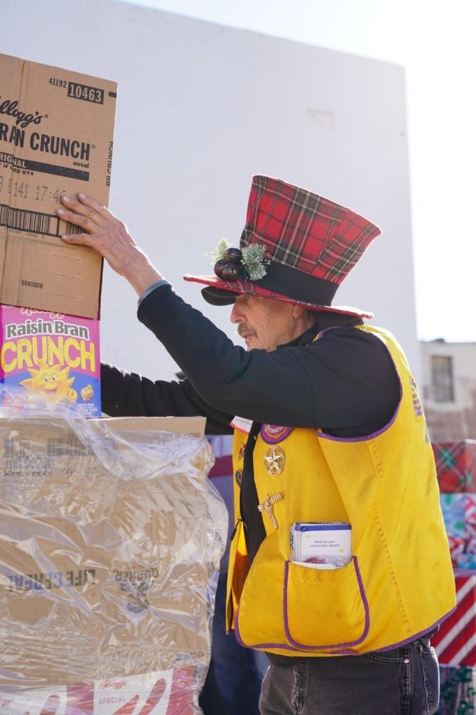 Person in yellow vest and red hat placing a cereal sign on a display table outdoors.