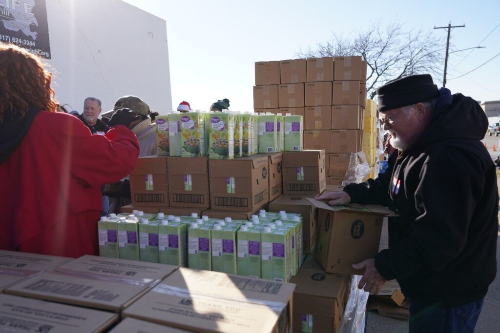 People sorting boxed canned goods at an outdoor food drive table in bright sunlight.