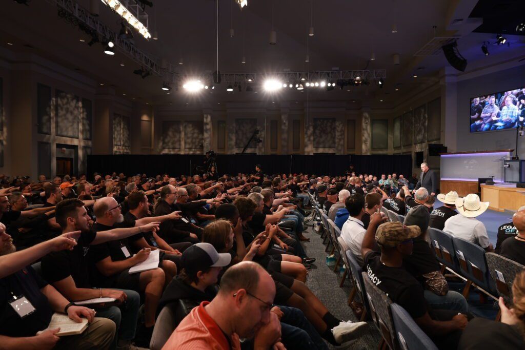 Audience seated in a large lecture hall, watching a presentation on stage