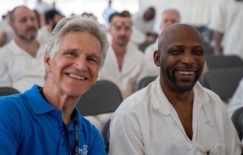 Two smiling attendees seated in a conference room, one in a blue polo and one in a white shirt