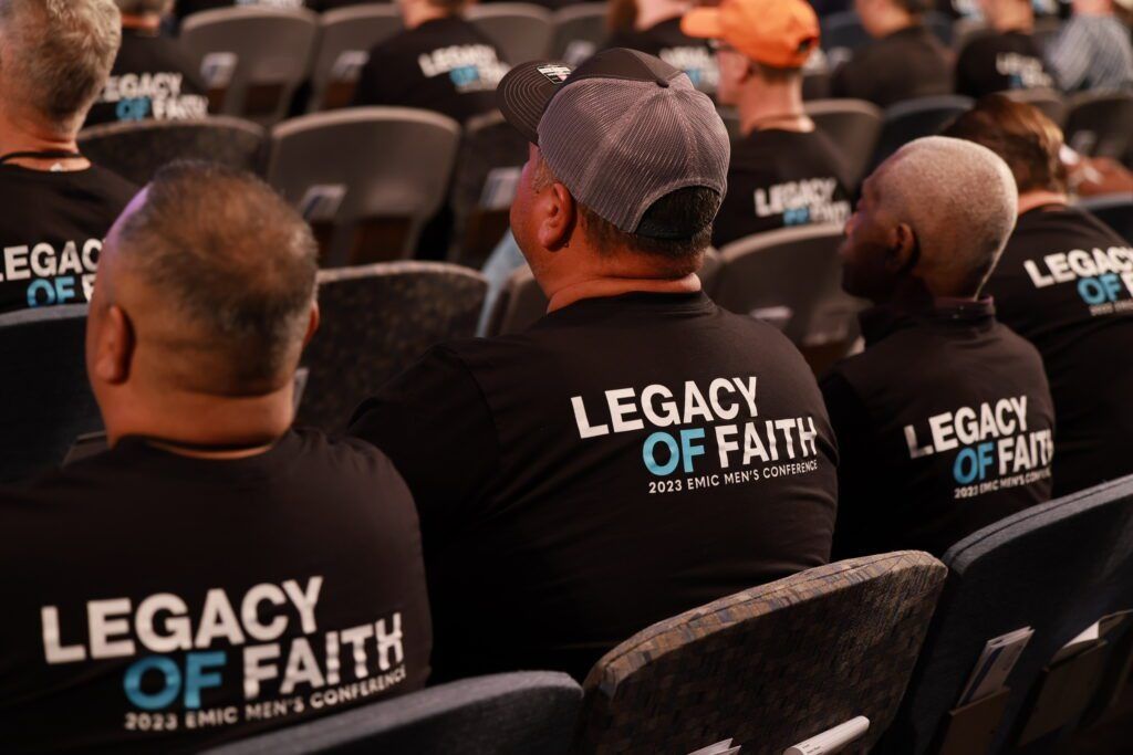 Audience seated at a conference wearing black “Legacy of Faith” shirts
