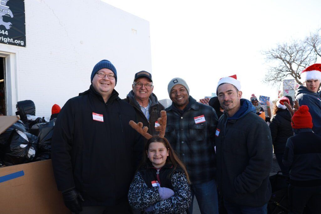 Five people posing outdoors in winter, smiling in front of a white wall and snow.