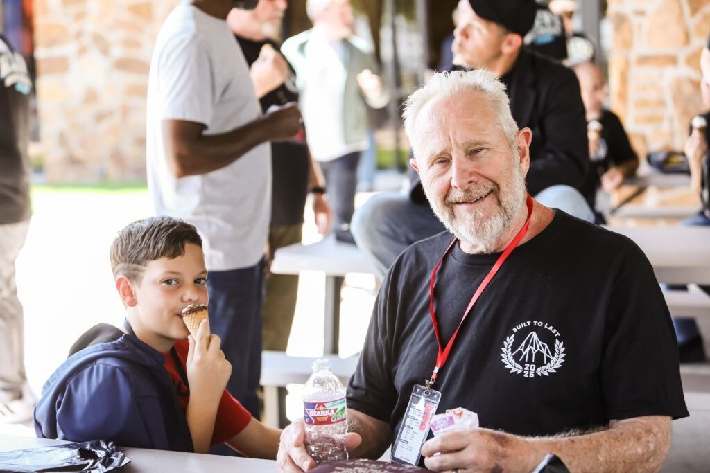 Older man and child seated at an outdoor table, smiling during a casual gathering.