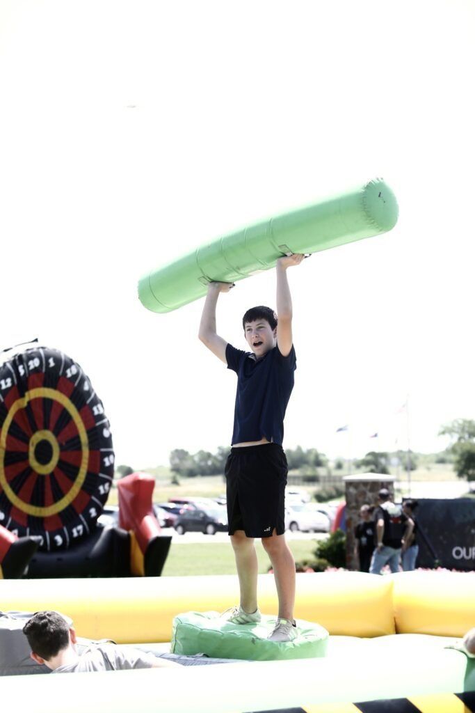 Person standing on a pedestal, holding a large green inflatable overhead at an outdoor event.