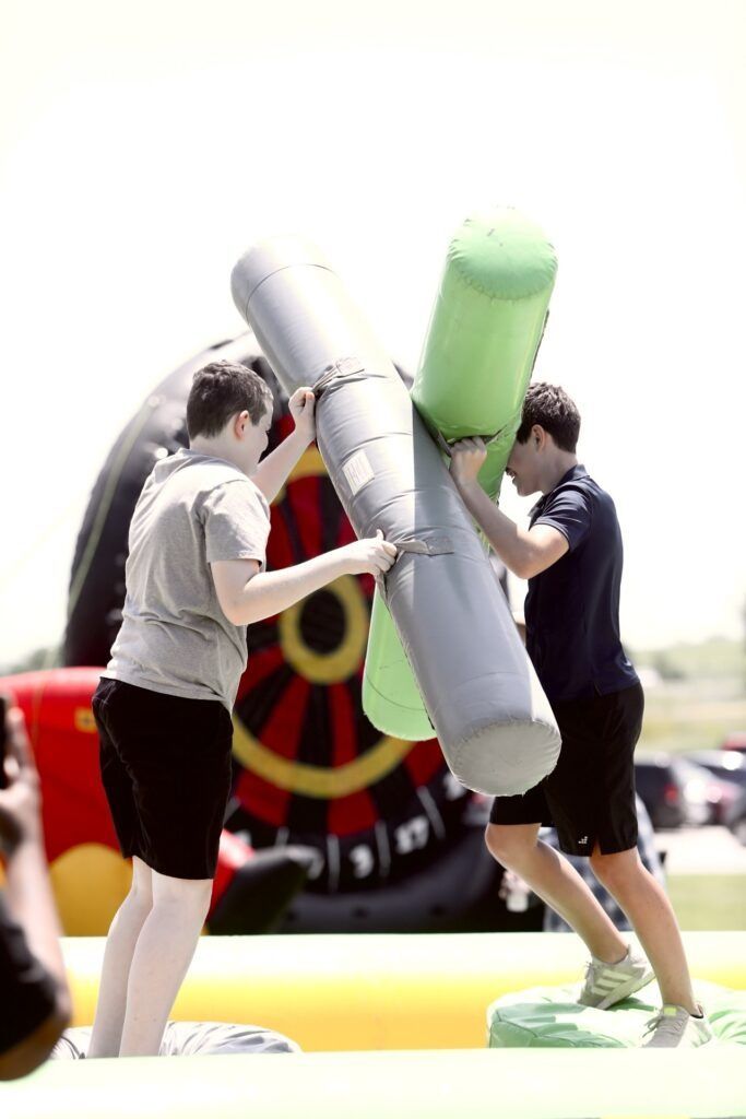 Two people sparring in padded sticks during an outdoor inflatable obstacle game