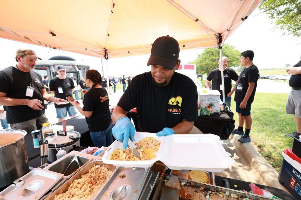 Food vendor serving pasta at an outdoor event under a canopy