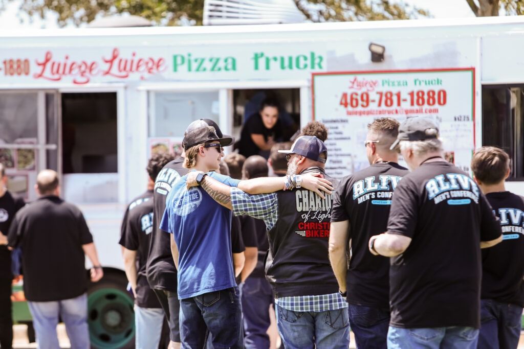 People gathered in front of a colorful pizza truck with a large order sign.