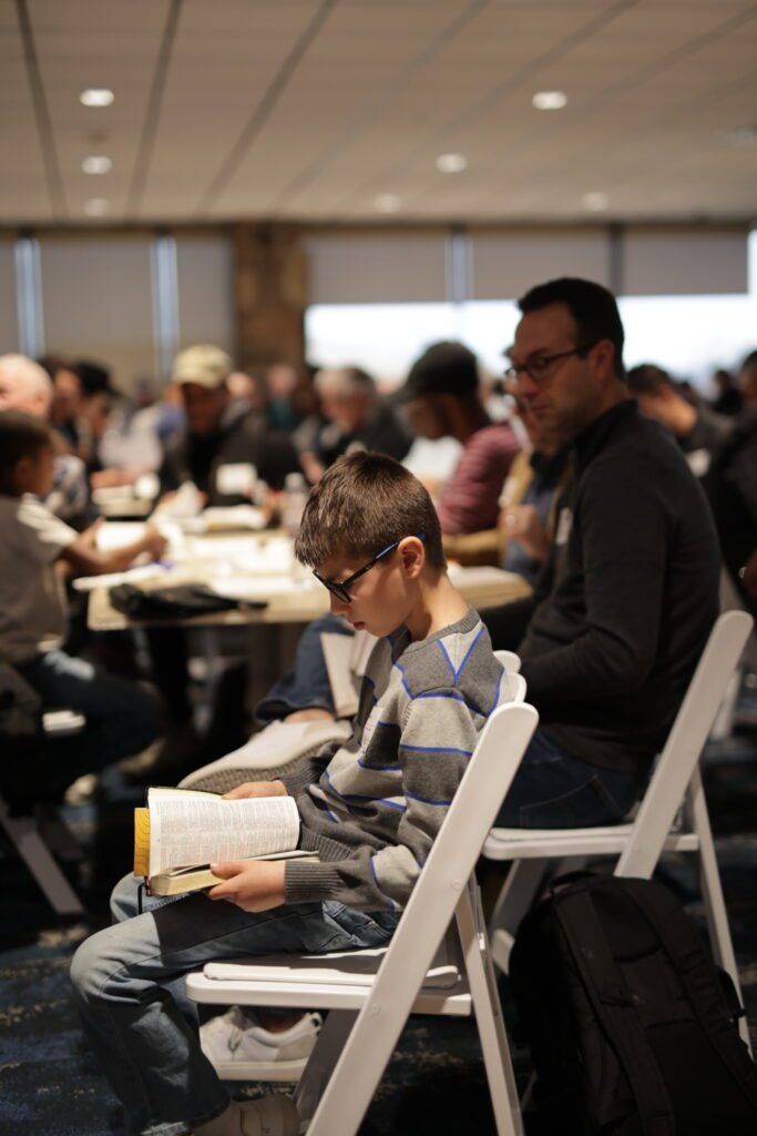 Audience seated at a conference, with a child reading a booklet in the foreground