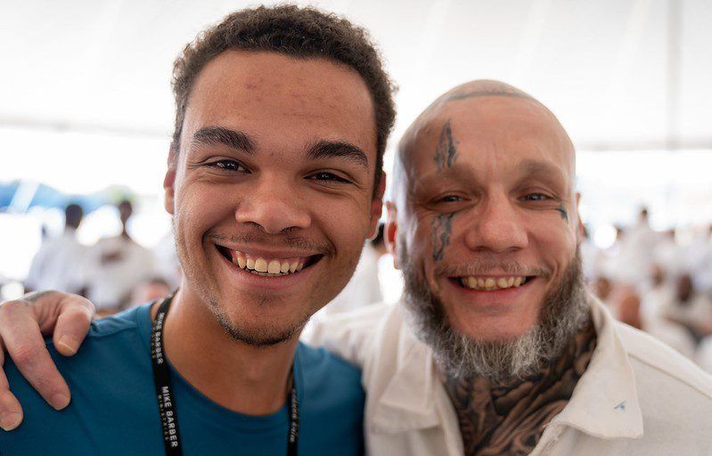 Two smiling people posing together indoors, one in a blue shirt and one in a white shirt.