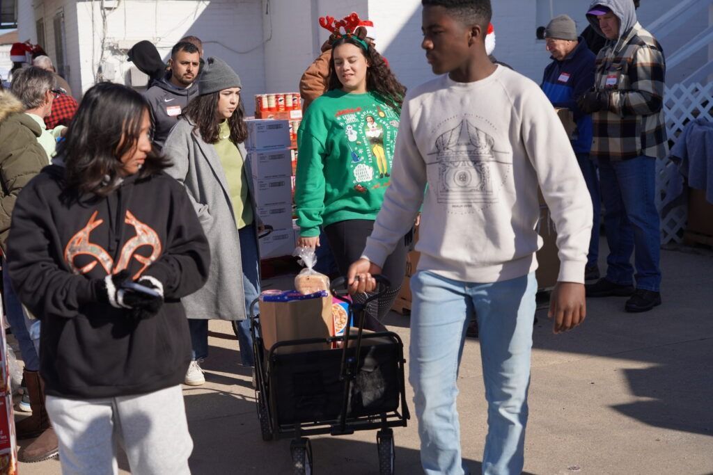 People walking outdoors with a rolling suitcase and holiday decorations in the background