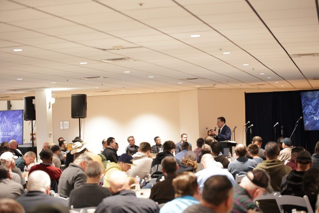 Conference audience seated in a large hall, facing speakers at the front.