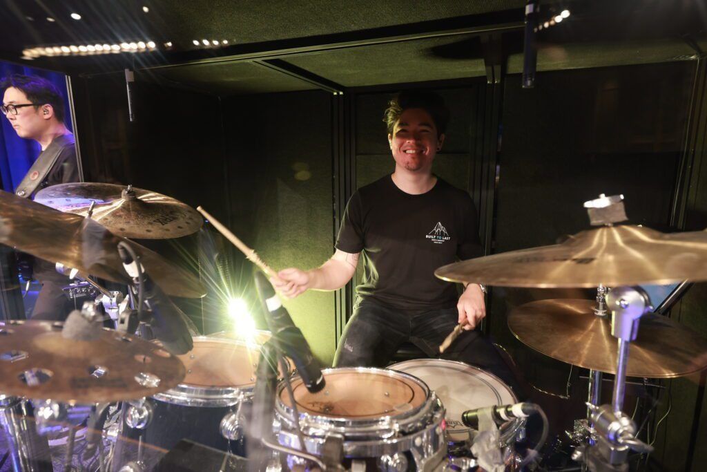 Drummer performing on stage under bright lights, surrounded by cymbals and drums