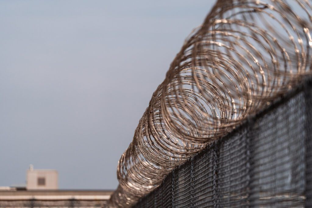 Barbed wire coils atop a chain-link fence against a pale sky