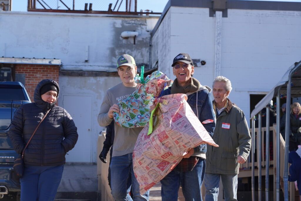 Four people standing outside a building, holding a colorful wrapped gift and smiling.