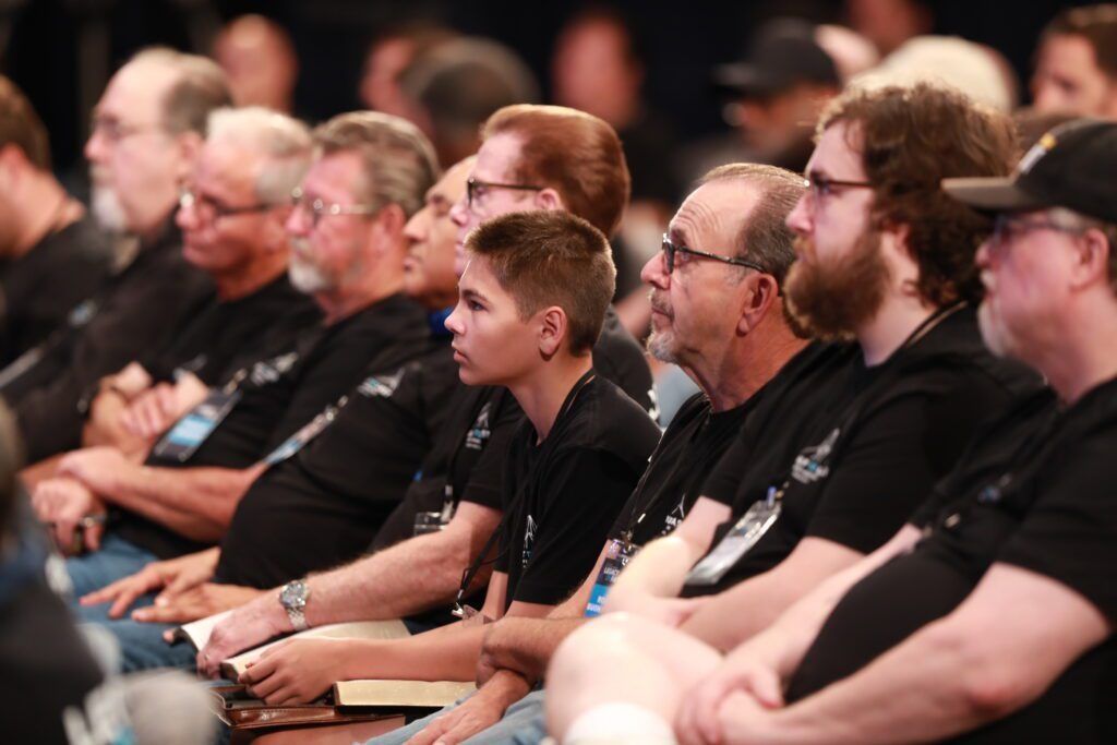 Audience seated at a conference, listening attentively in a dimly lit auditorium