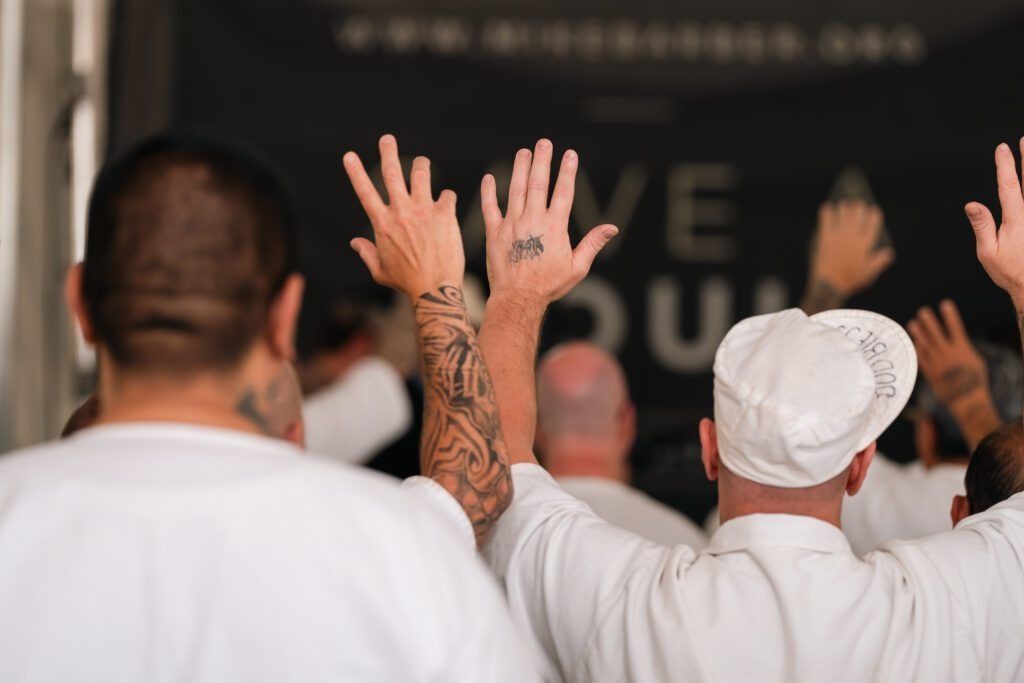 Audience with raised hands at a live event, seen from behind on a stage-facing view.