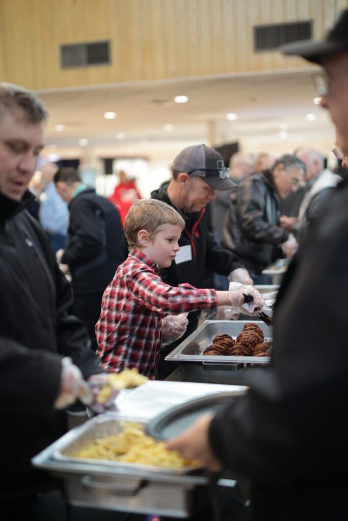 People serving food at a buffet line in a busy indoor hall