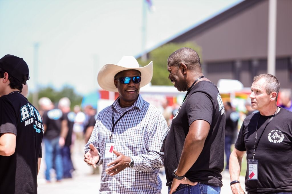 Three people chatting outdoors, one wearing a white cowboy hat and sunglasses.