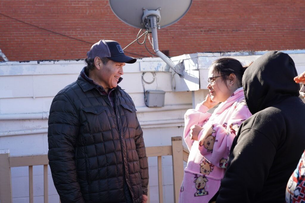 Three people talking on a rooftop by a satellite dish in bright sunlight.