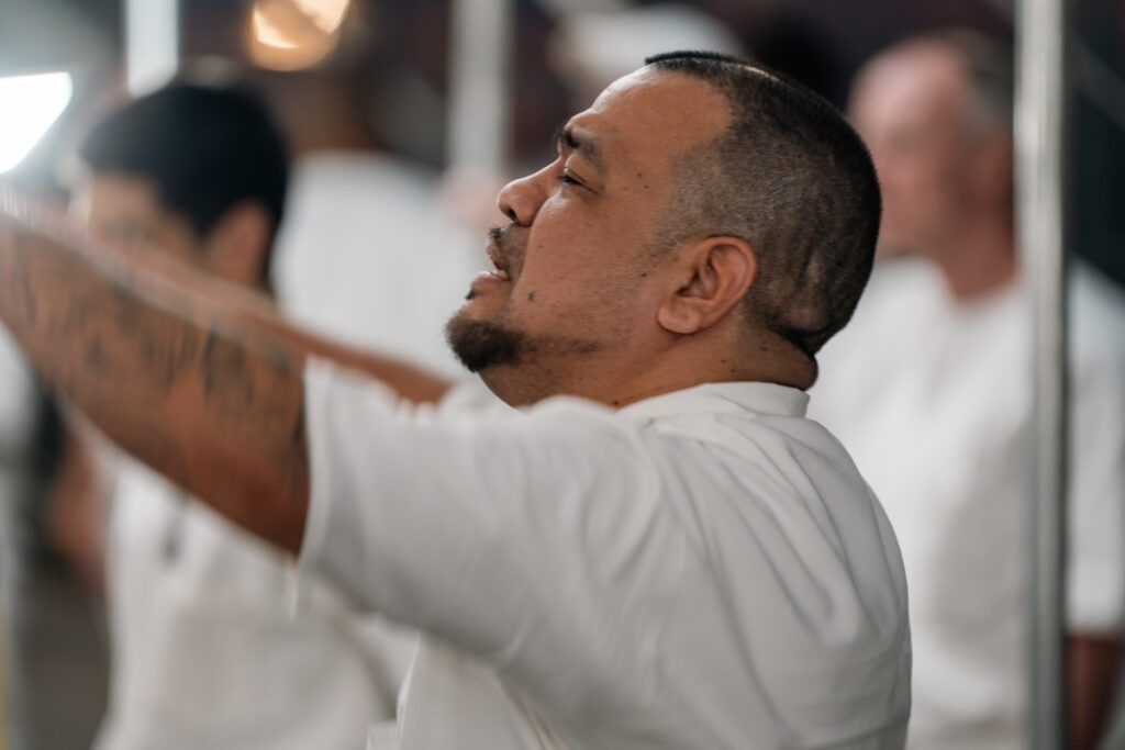Man in a white shirt reaching upward indoors, focused in a bright, blurred setting