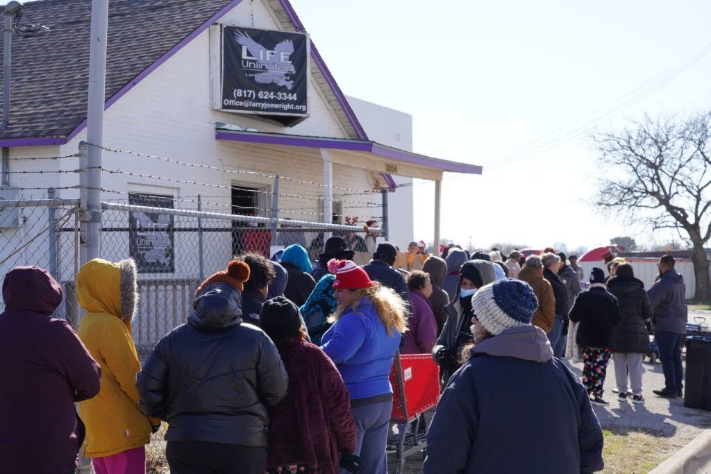 Crowd lines up outside a small storefront on a cold day, with people in winter coats facing the entrance.