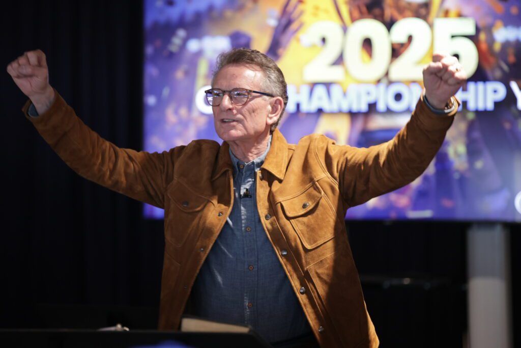 Speaker with arms raised on stage in front of a “2025 Championship” screen