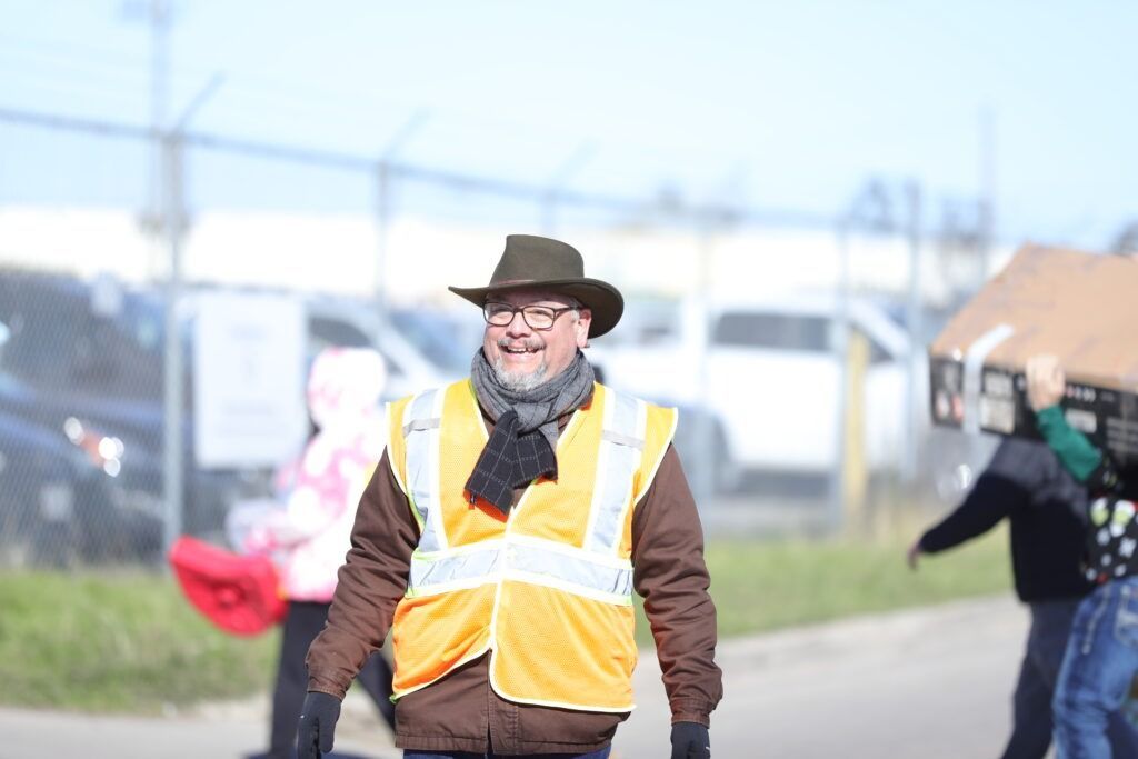 Man in orange safety vest and hat smiling outdoors at a roadside event