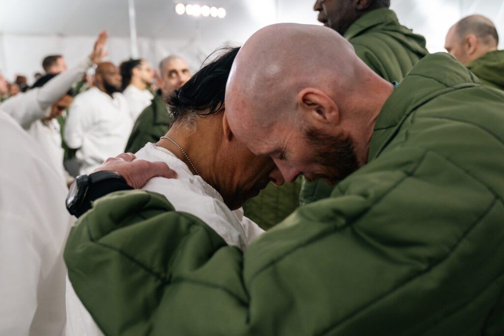 People in white and green embrace closely in a bright indoor setting