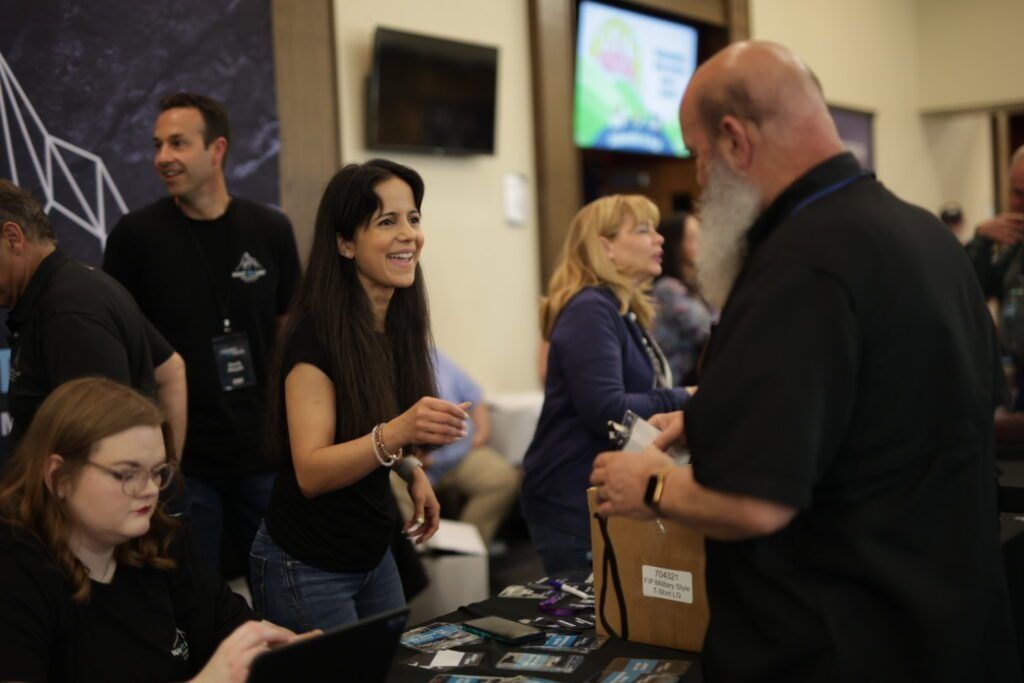 People chatting at a booth indoors, with a woman smiling beside a display table.
