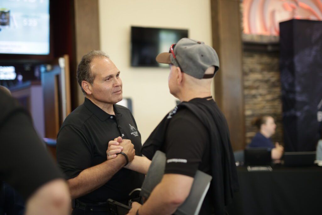 Two men talking in a convention hall, one holding a microphone and the other wearing a gray cap.