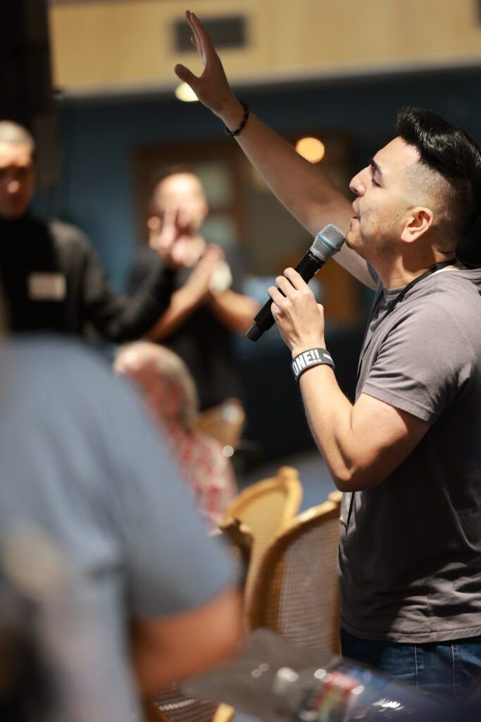 Man speaking into a microphone and raising a hand during a seated audience event