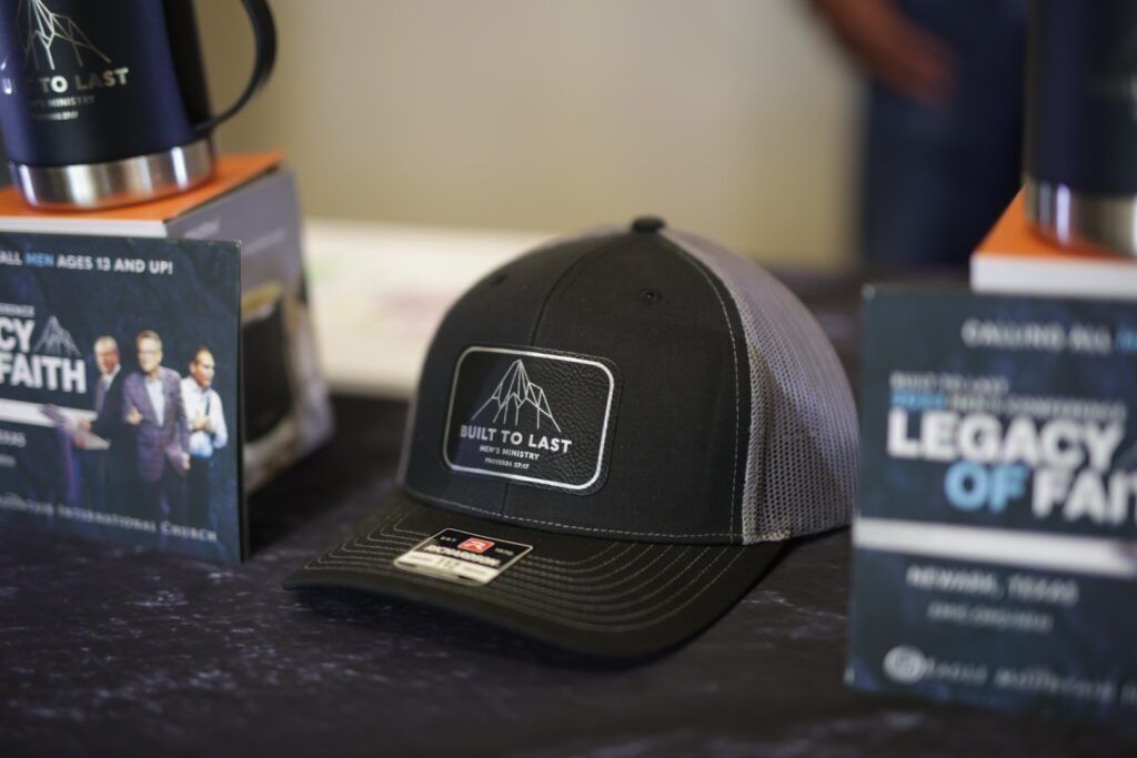 Black mesh cap on a table between two promotional signs, one reading “Legacy of Faith.”