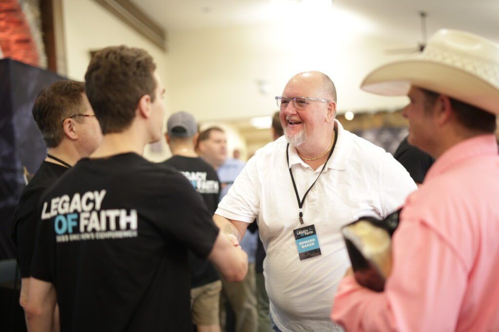 People chatting at an indoor event, with a man in a white shirt smiling at center.