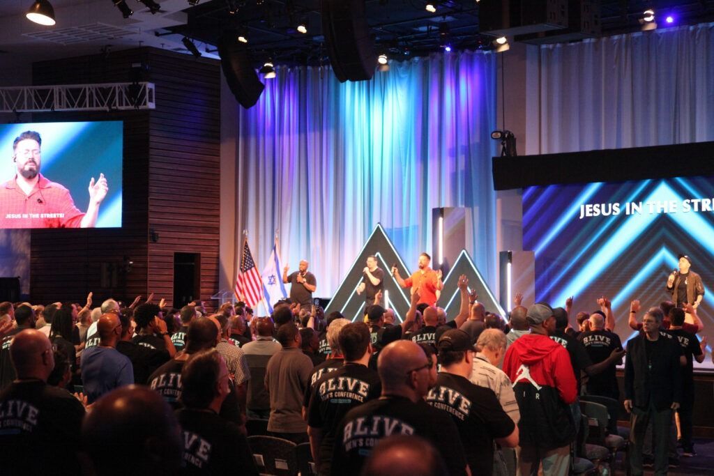 Crowd worshiping at a church conference stage with blue lights and large screen display
