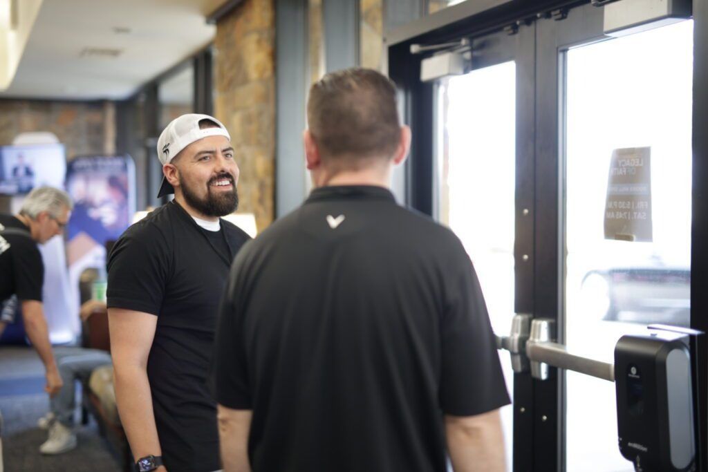 Two men chatting near a glass entrance in a gym or office lobby