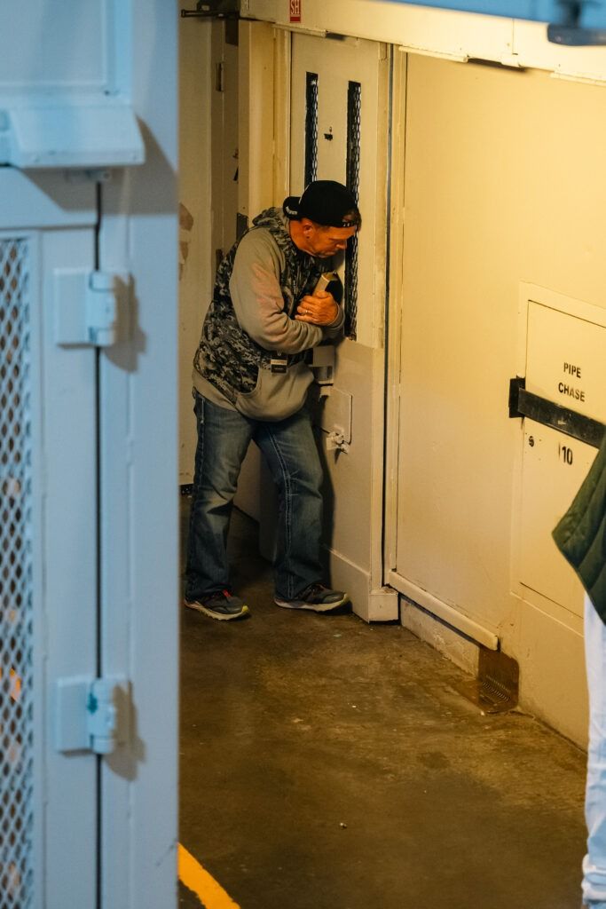 Person in a narrow hallway, bent over and holding their face near a wall-mounted fixture.