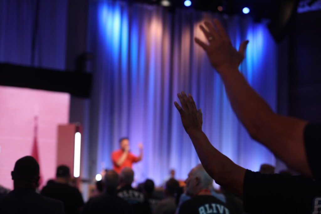 Audience raising hands at a blurred stage event with blue and purple lights
